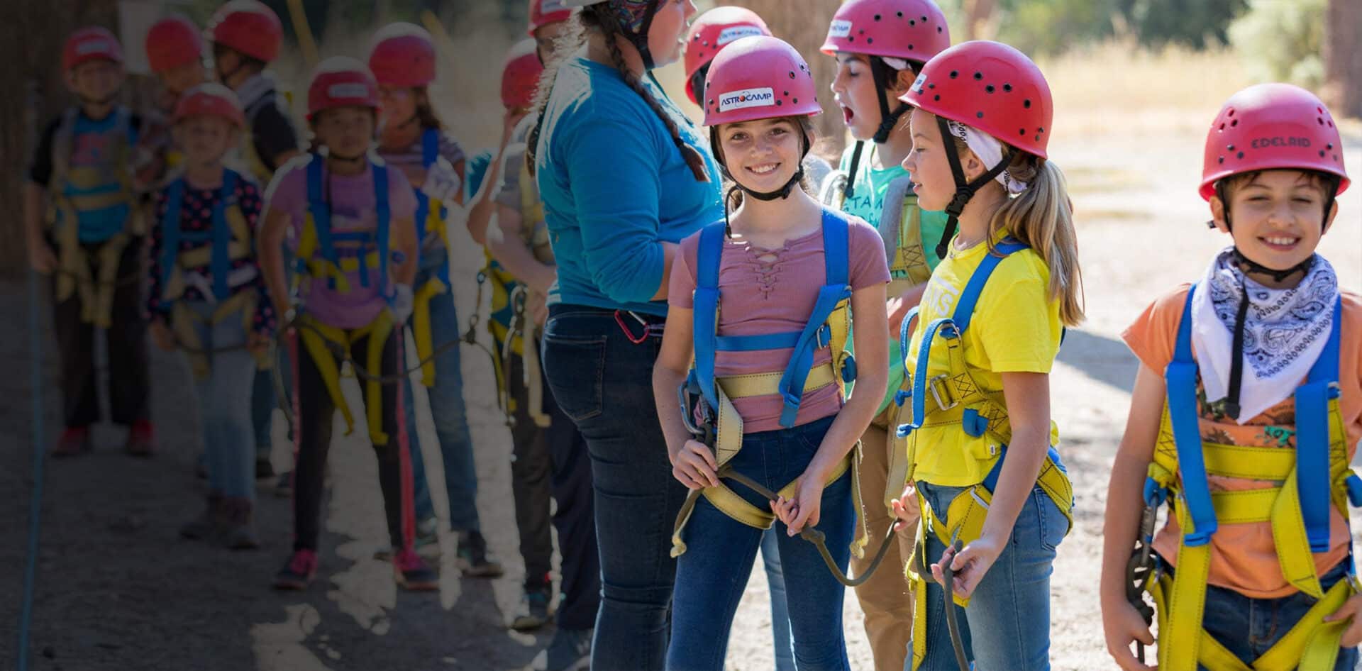 Kids standing in line smiling with zipline gear.