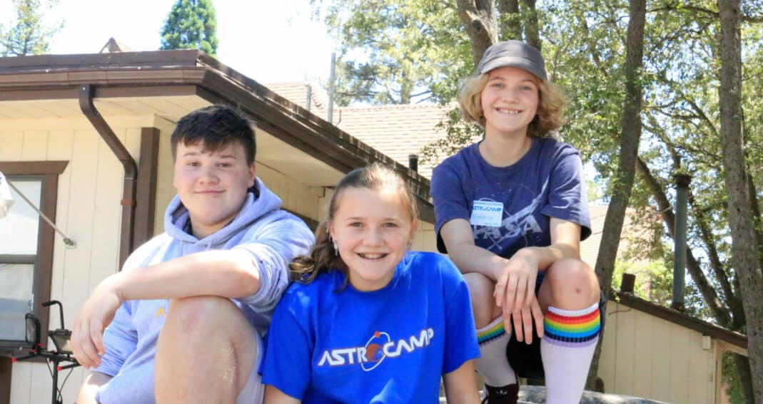 Three kids sitting on rock.