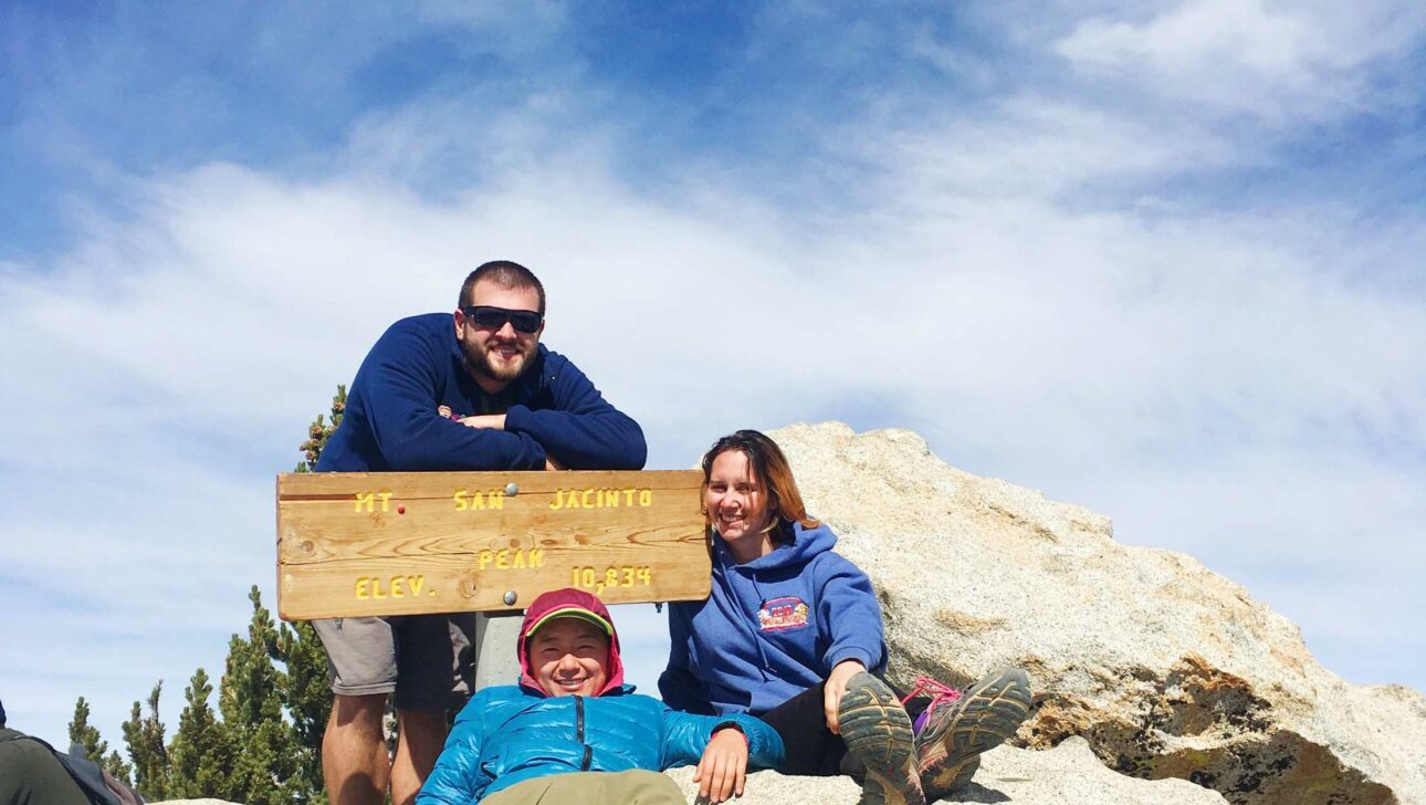 Three people around sign on rock.